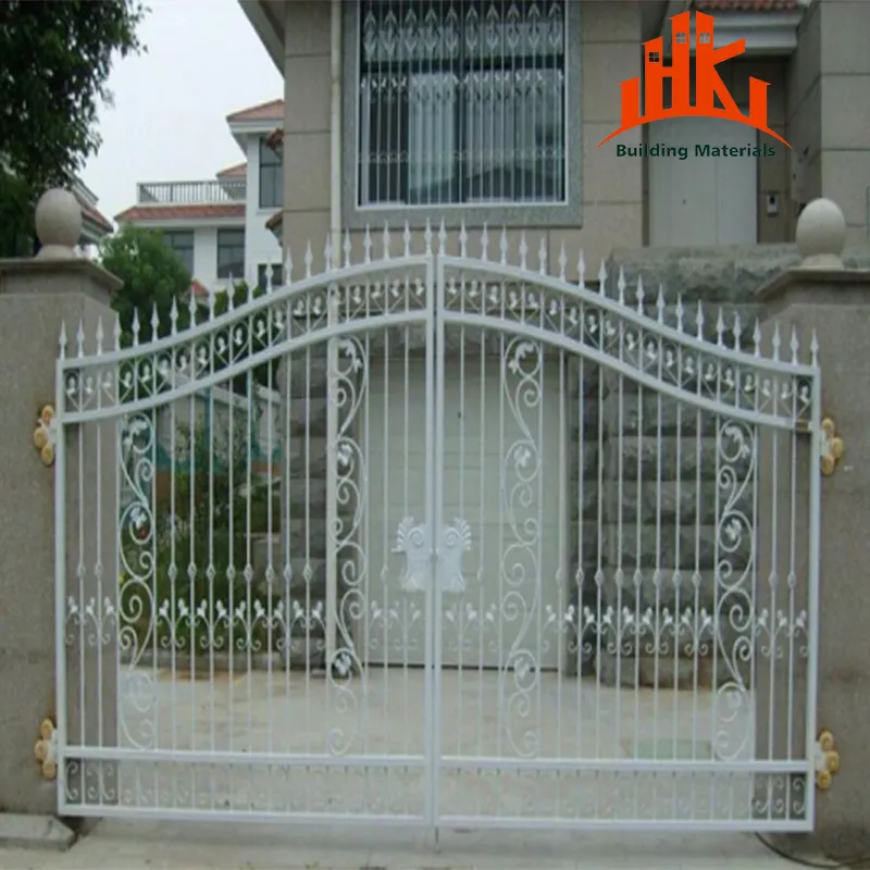 A white, ornamental double-swing driveway gate installed between stone pillars in front of a house.