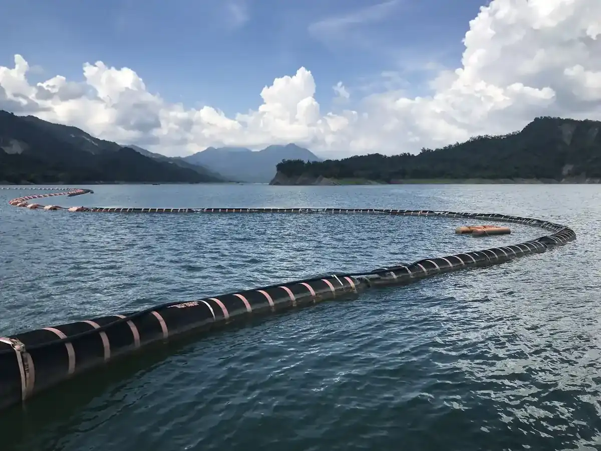 Floating dredging pipeline curving across a reservoir between forested hills