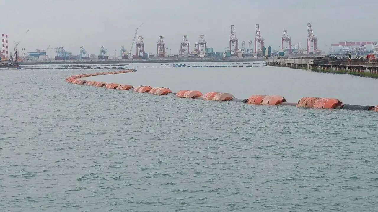 Floating dredging pipeline with orange PE floats running past container port cranes