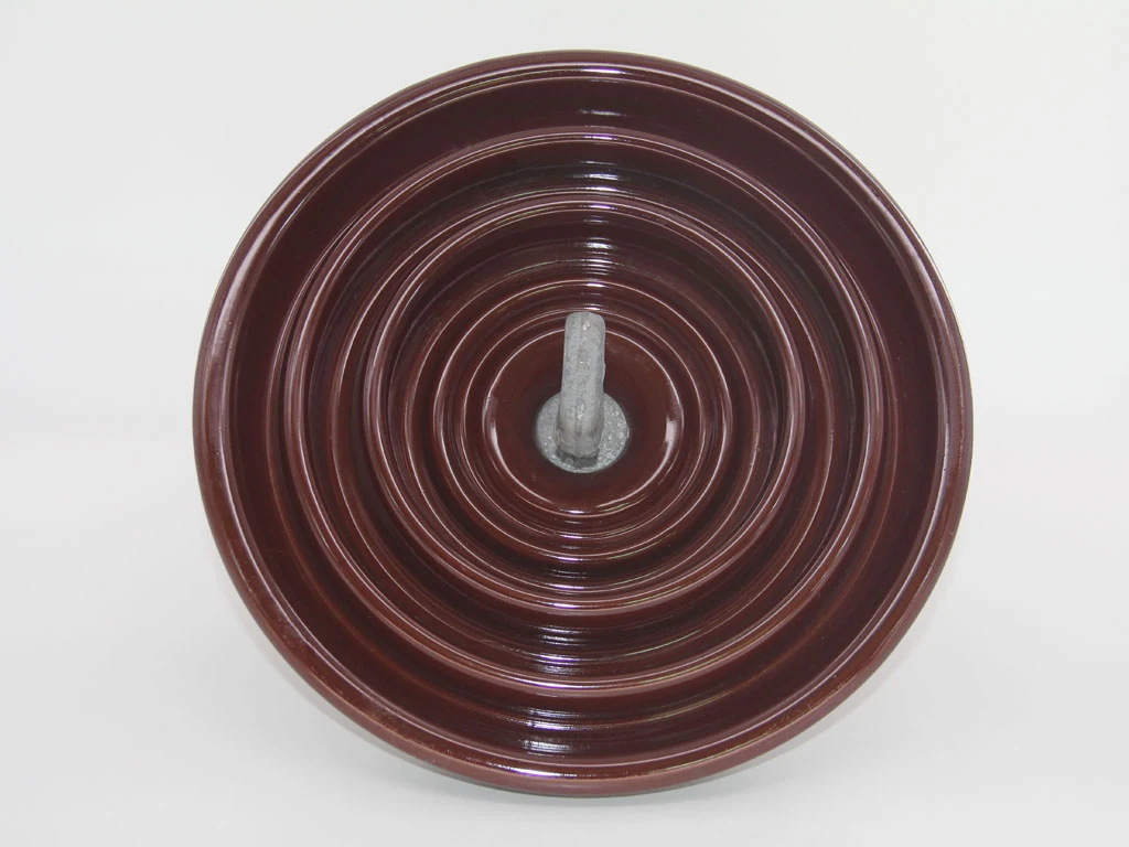 Brown glazed porcelain disc insulator with central metal pin, viewed from above on a plain light