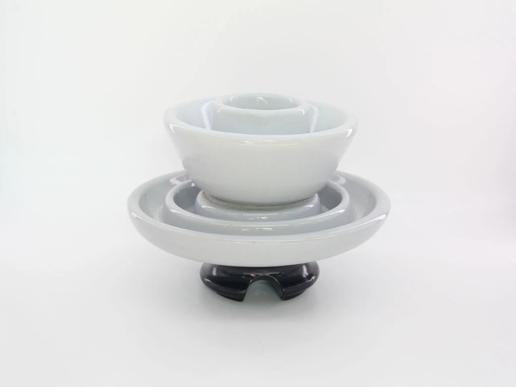Glossy white glazed ceramic insulator with stacked conical sheds on a dark base, centered on a plain white background