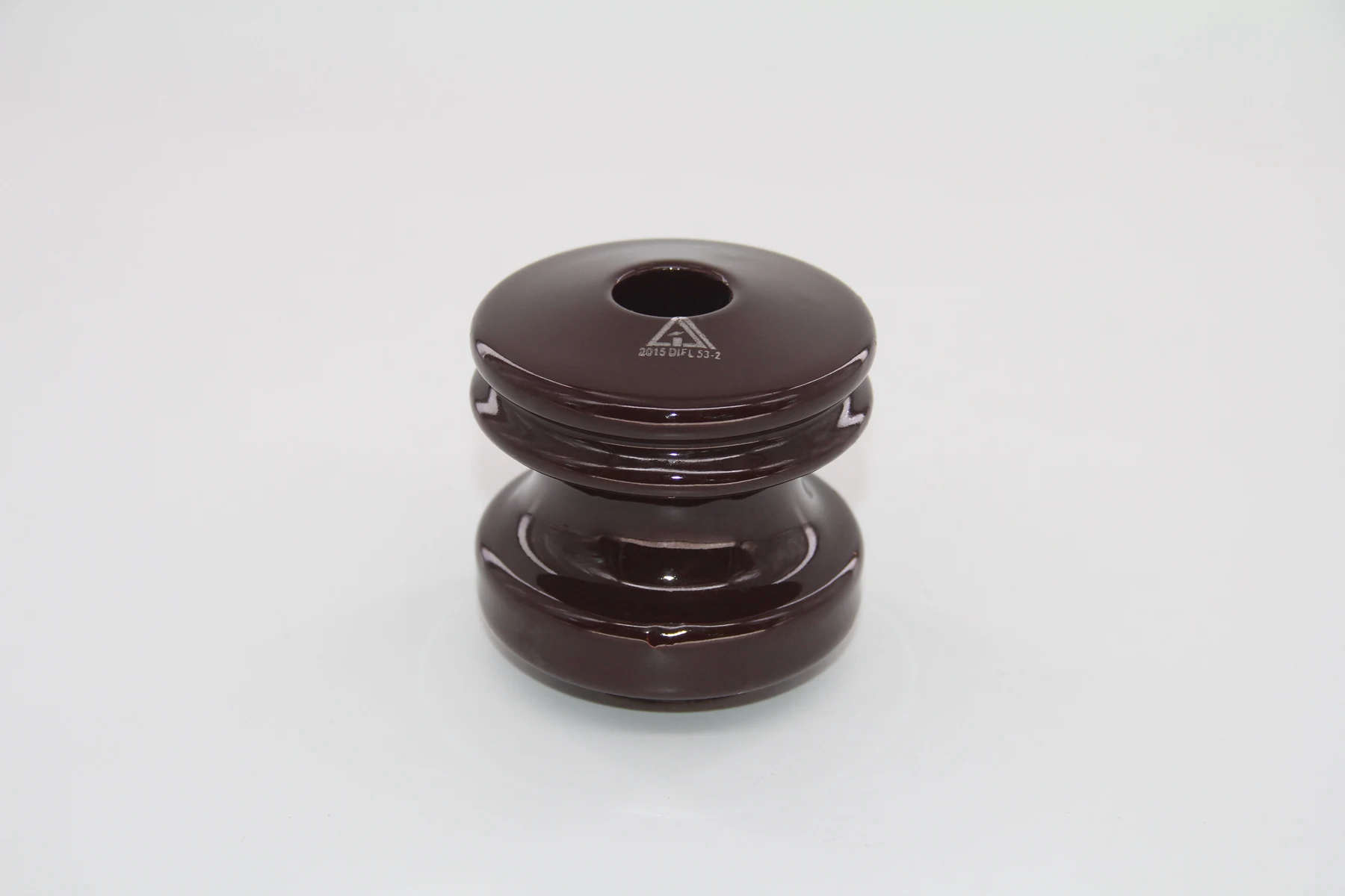 A brown ceramic insulator with a central hole and grooved middle section against a white background.