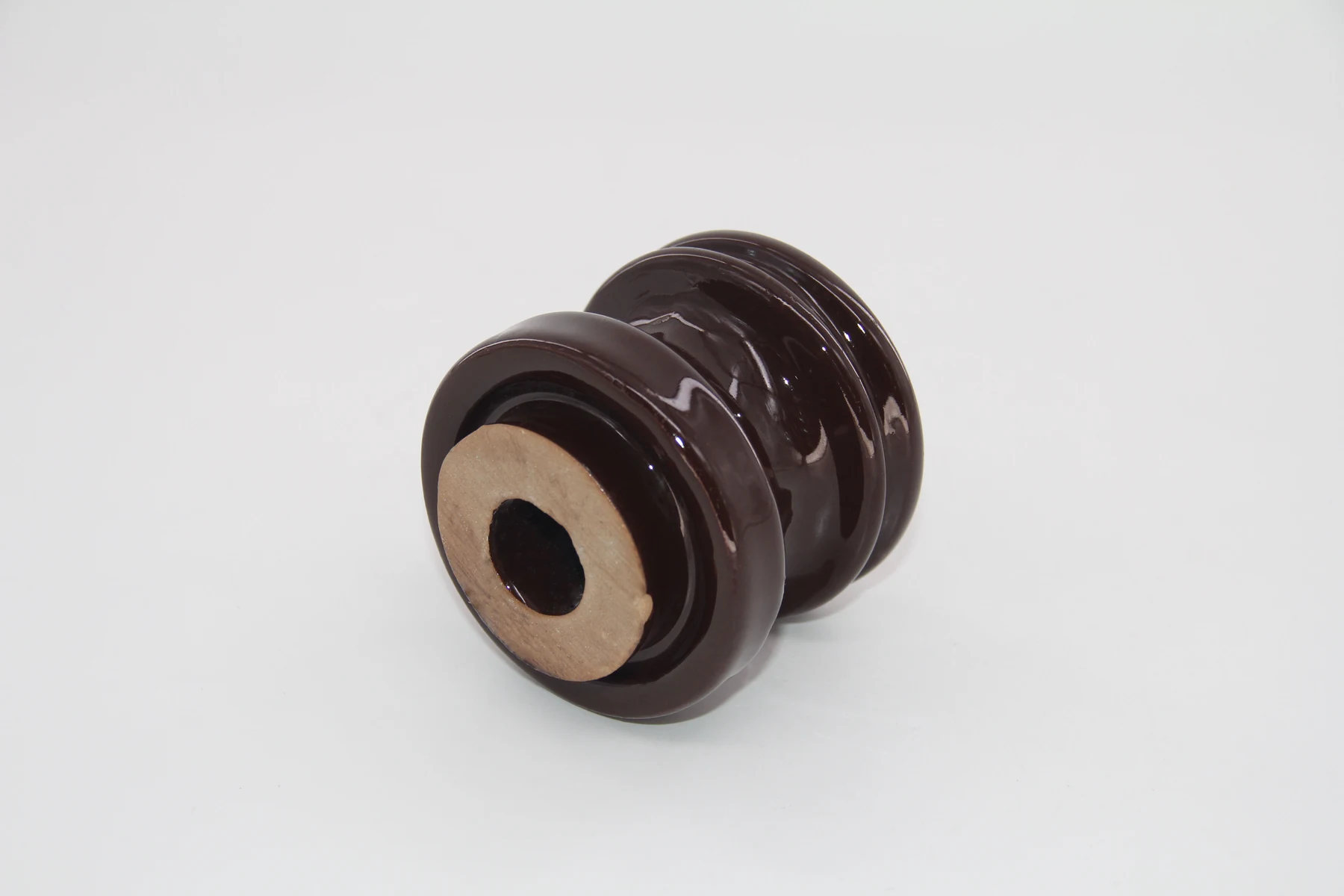 Brown glazed porcelain electrical insulator with central mounting hole lying on its side on a white background