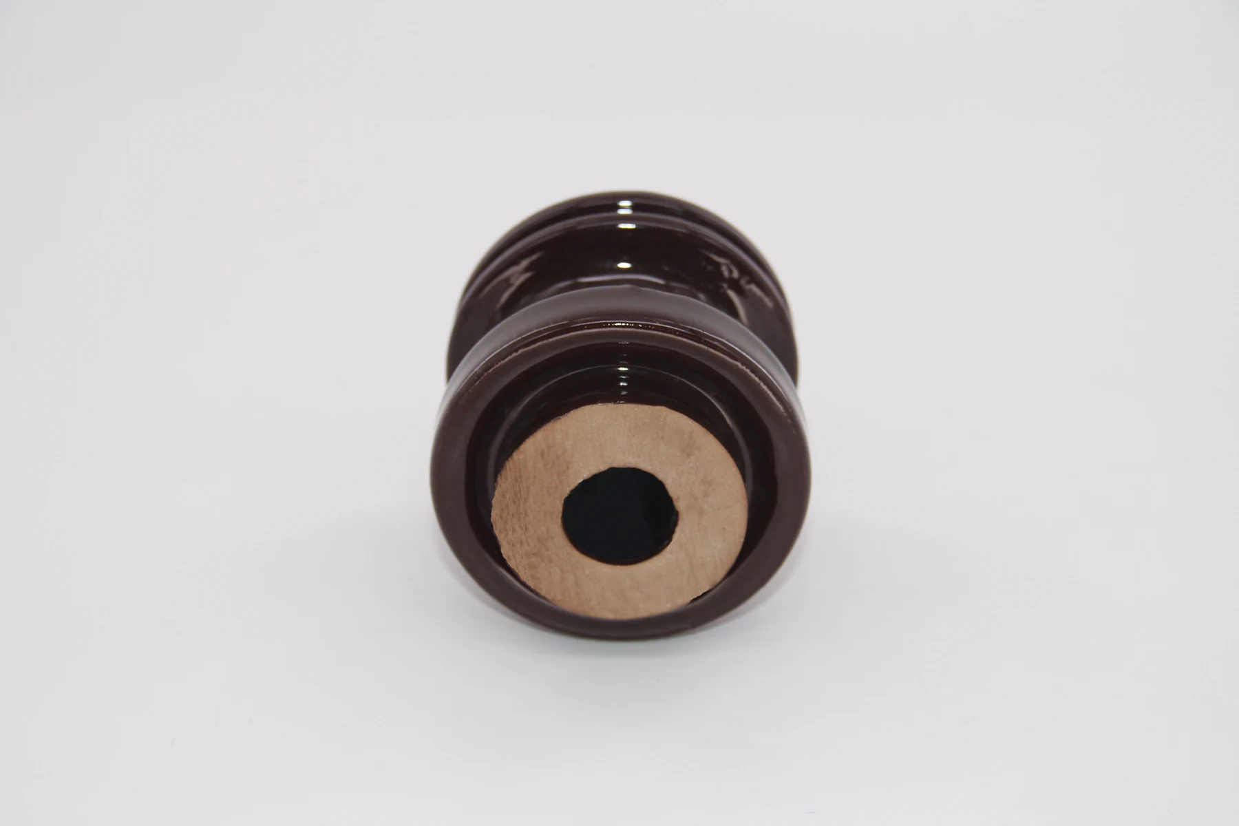 Brown glazed ceramic insulator with a central bore and beige rim, photographed upright on a plain white background