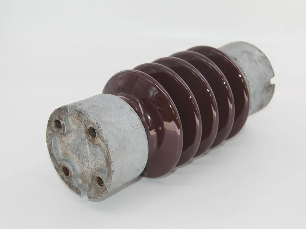 Brown glazed porcelain electrical insulator with cast metal end fittings lying on a white background