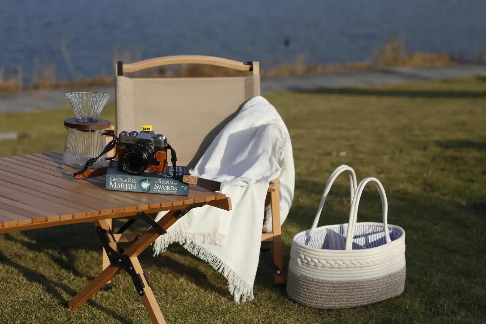 Mango folding camping table and rope basket bag laid out on a lakeside lawn