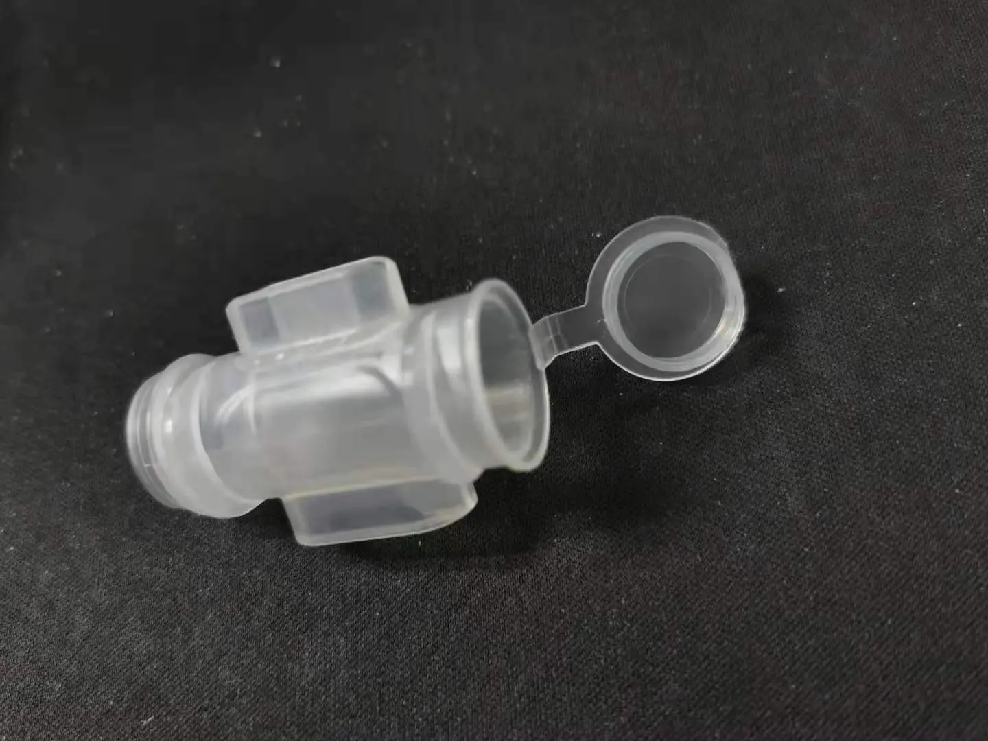 Clear molded valve body with a tethered cap, as molded
