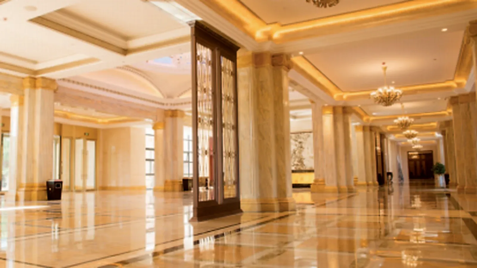 Gold chandeliers lighting a marble hotel lobby