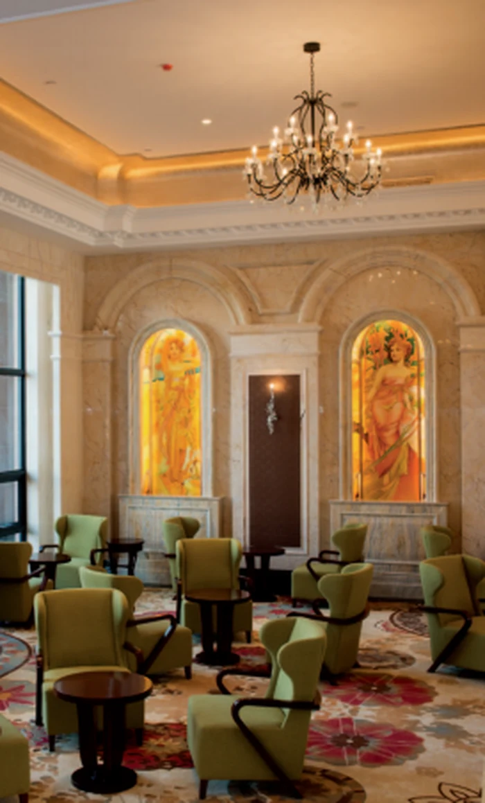 Chandelier above a hotel lounge with green armchairs and stained glass panels