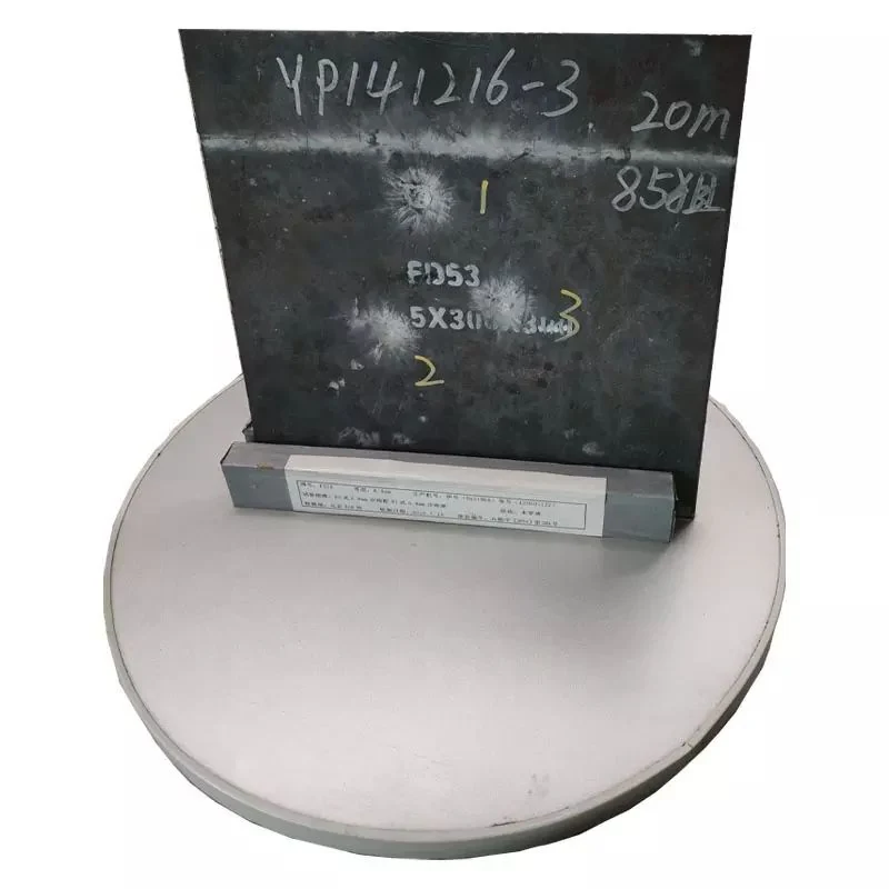 Dark steel plate sample with handwritten markings standing upright on a round metal base against a white background