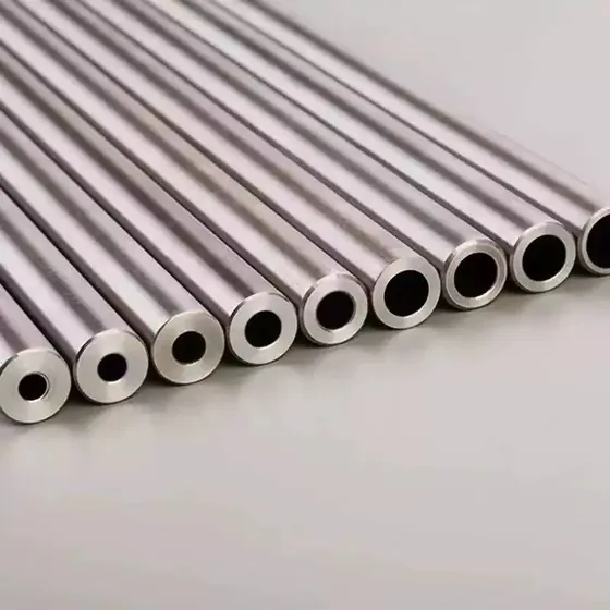 Row of polished hollow metal tubes with varying diameters arranged diagonally on a plain gray surface