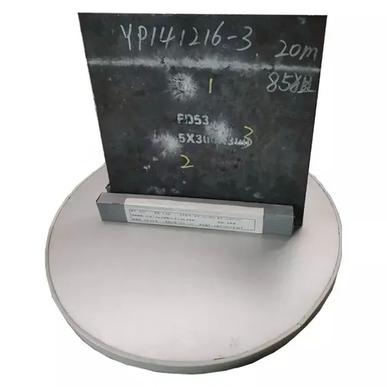 Dark steel plate sample with handwritten markings standing upright on a round metal base against a white background