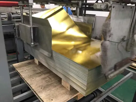 Stack of gold-coated metal sheets on a wooden pallet being fed through industrial processing machinery