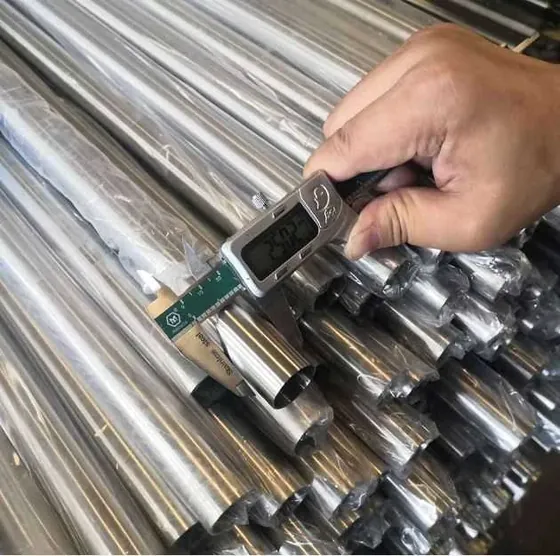Hand using a digital caliper to measure the diameter of a bundle of wrapped stainless steel pipes.
