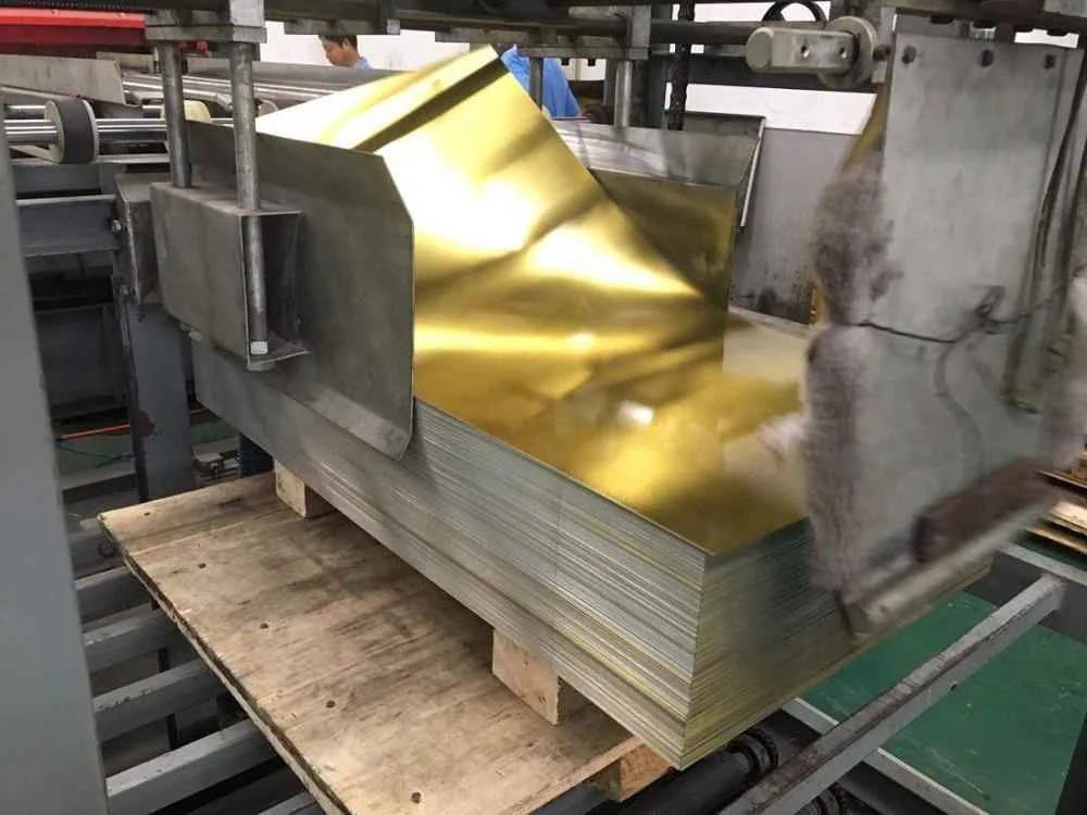Stack of gold-coated metal sheets on a wooden pallet being fed through industrial processing machinery