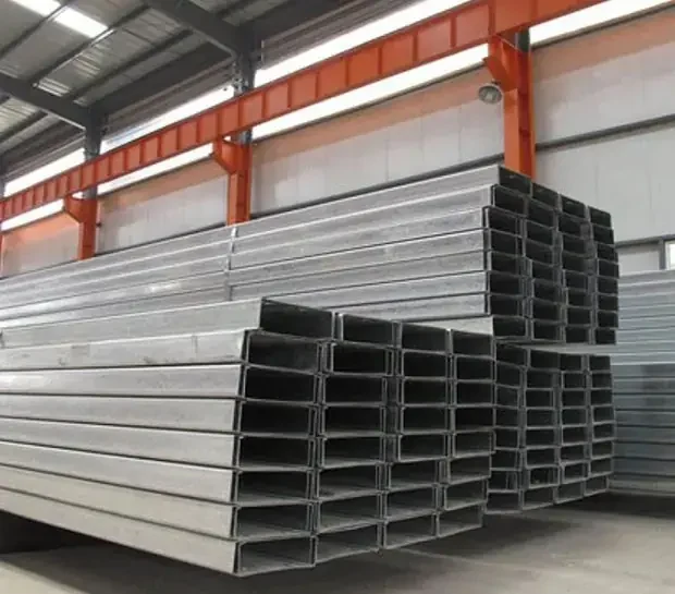 Stacks of galvanized steel C-channel profiles in an industrial warehouse with orange support beams