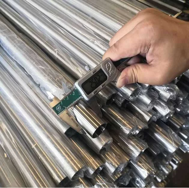 Hand using a digital caliper to measure the diameter of a bundle of wrapped stainless steel pipes.