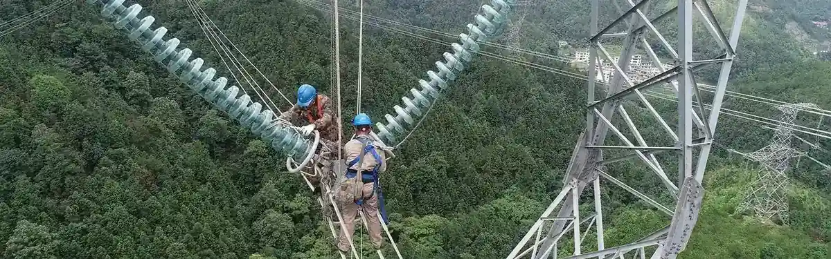 Linemen installing toughened glass insulator strings on a high voltage transmission tower