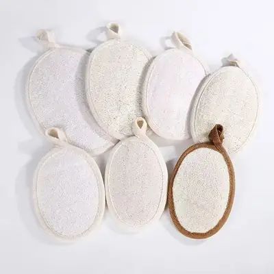 Loofah pad in use during body scrubbing, showing the elastic strap and grip