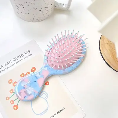 Brush held in hand showing its compact size and rounded teeth
