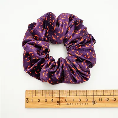 Multiple scrunchies laid out showing the pumpkin and bat design in different colours