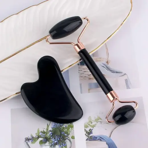 Gua Sha and jade roller tools laid out on a white surface with natural stone texture