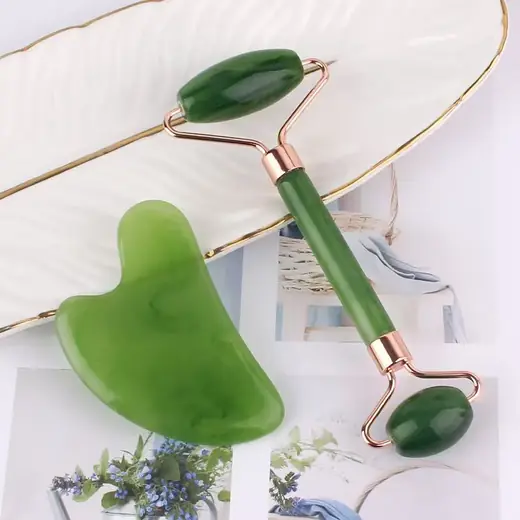 Jade roller and Gua Sha tool set laid out on a white surface with natural stone texture visible