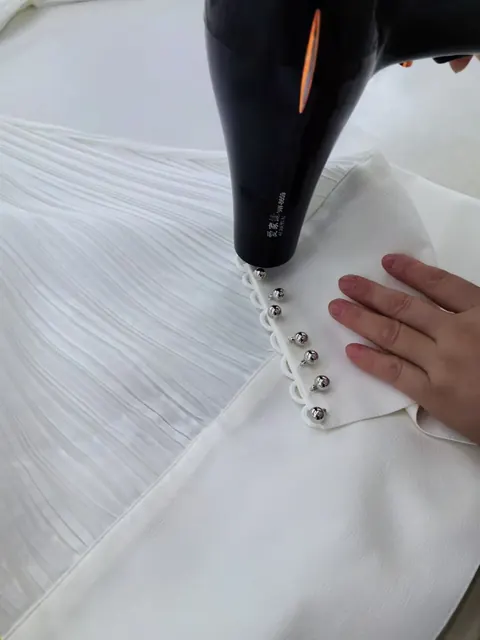 Steaming a pleated ivory blouse with covered buttons during final pressing