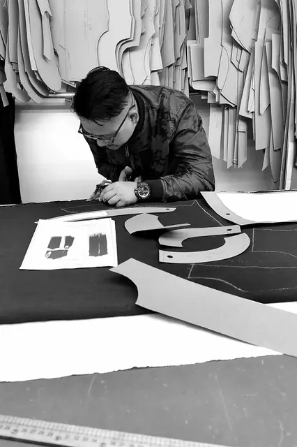 Pattern maker cutting a marker over black fabric under hanging paper patterns