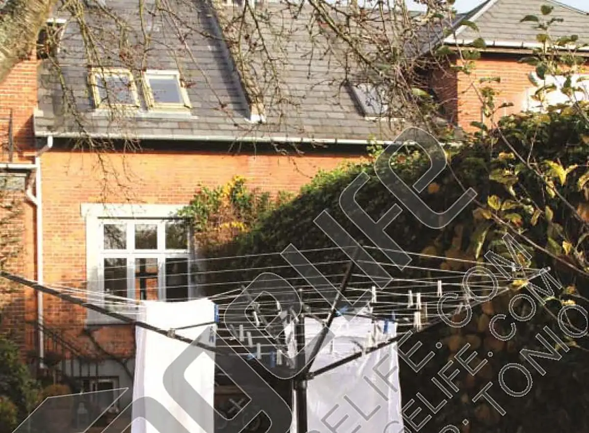 Rotary airer loaded with white laundry outside a brick house