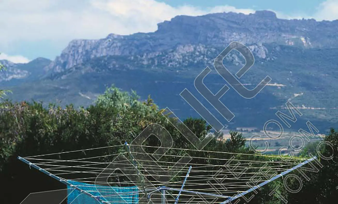 Four-arm aluminium rotary airer open in a garden below a mountain ridge