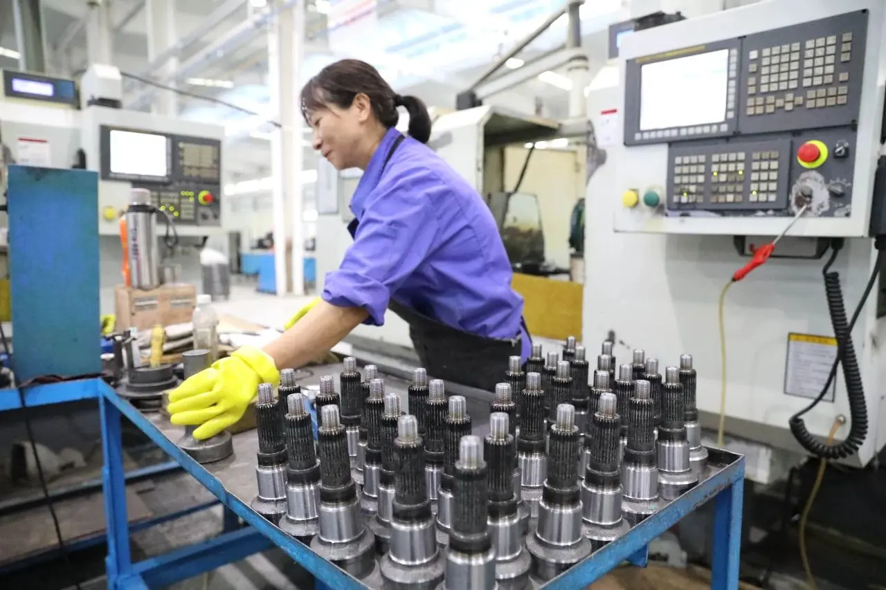 Machine operator loading finished shaft components onto a trolley beside a CNC lathe