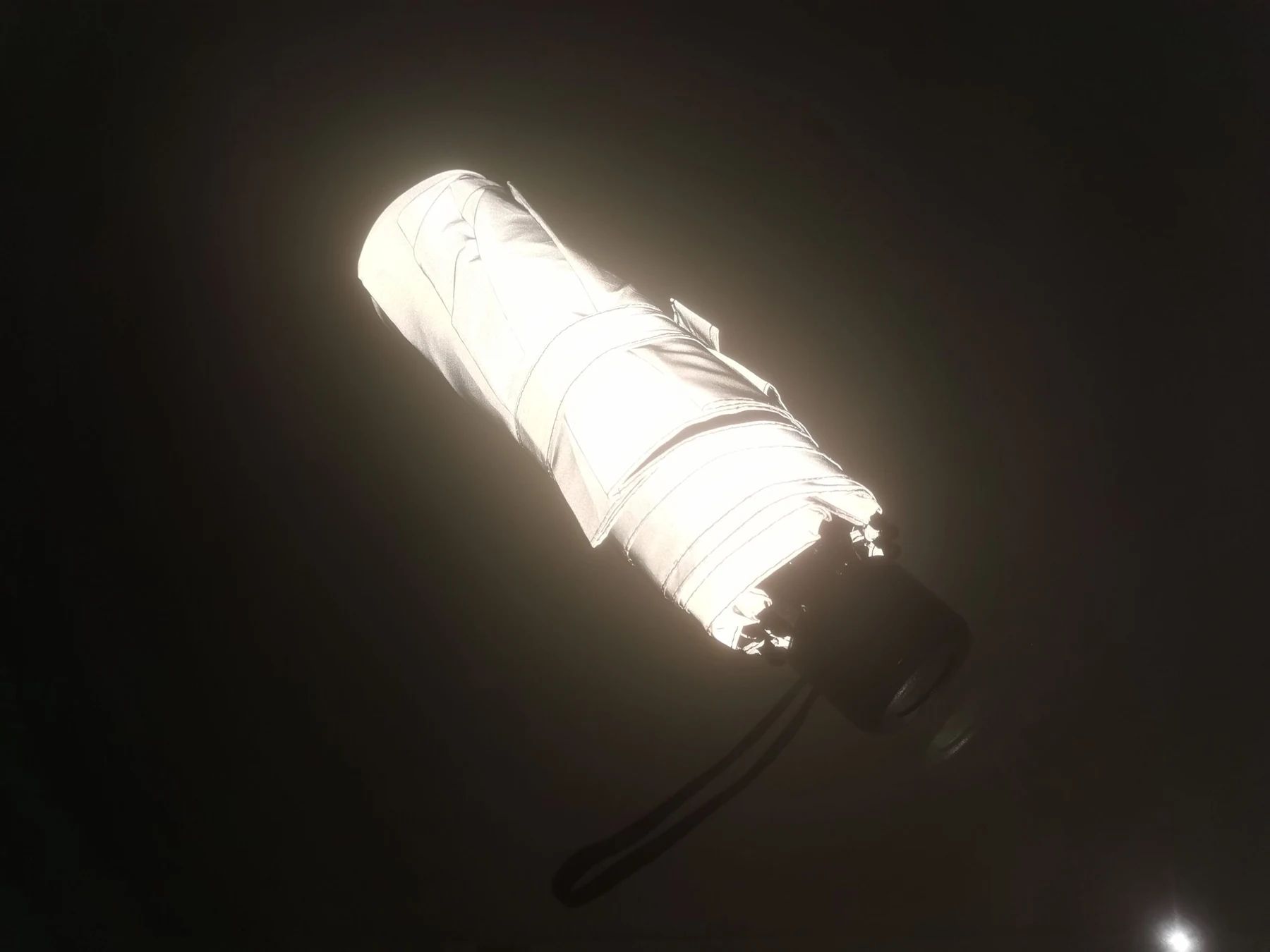 Closed reflective folding umbrella returning light in a dark room