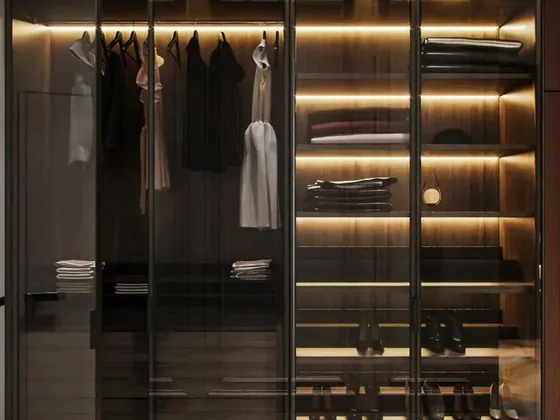 Walk in wardrobe with hanging rails lit by concealed LED strip lighting
