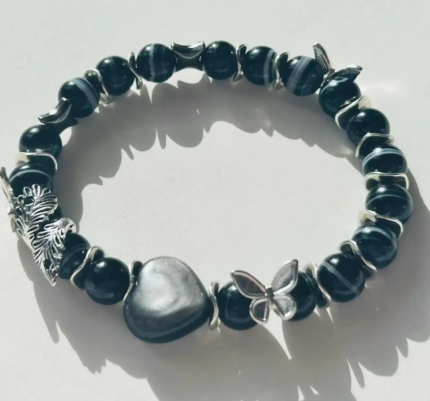 Feather of Purity black Persian agate and silver obsidian crystal bracelet, the bracelet styled on a surface