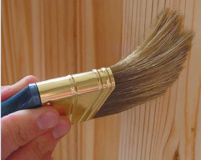 Brush applying a clear coating to a pine wood panel