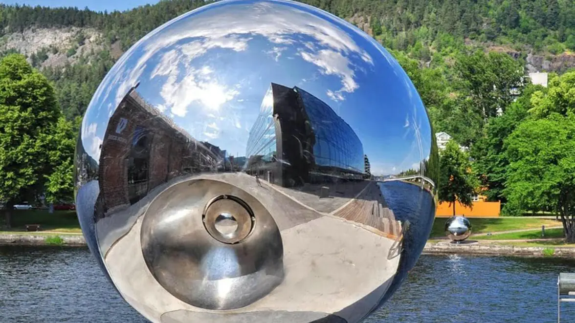 A mirror polished large steel sphere installed on a river bank in Poland