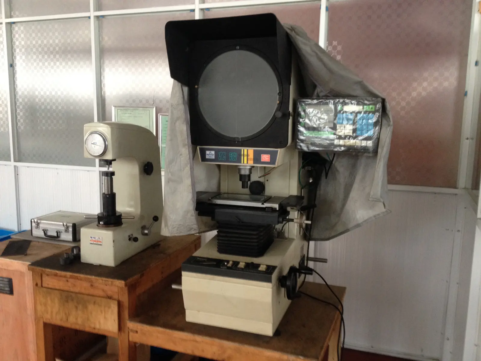 Optical comparator and hardness tester on wooden workbenches in a workshop
