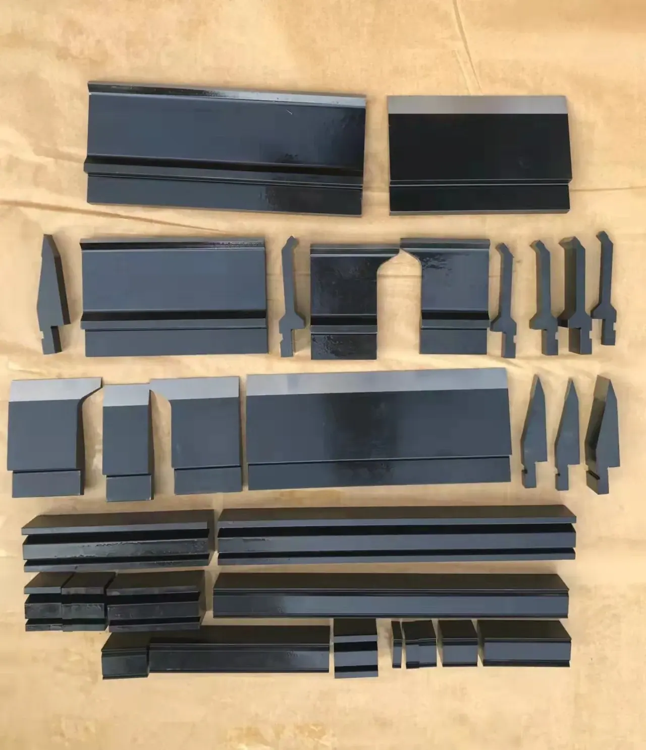 Set of black metal press brake tooling dies arranged on a tan surface