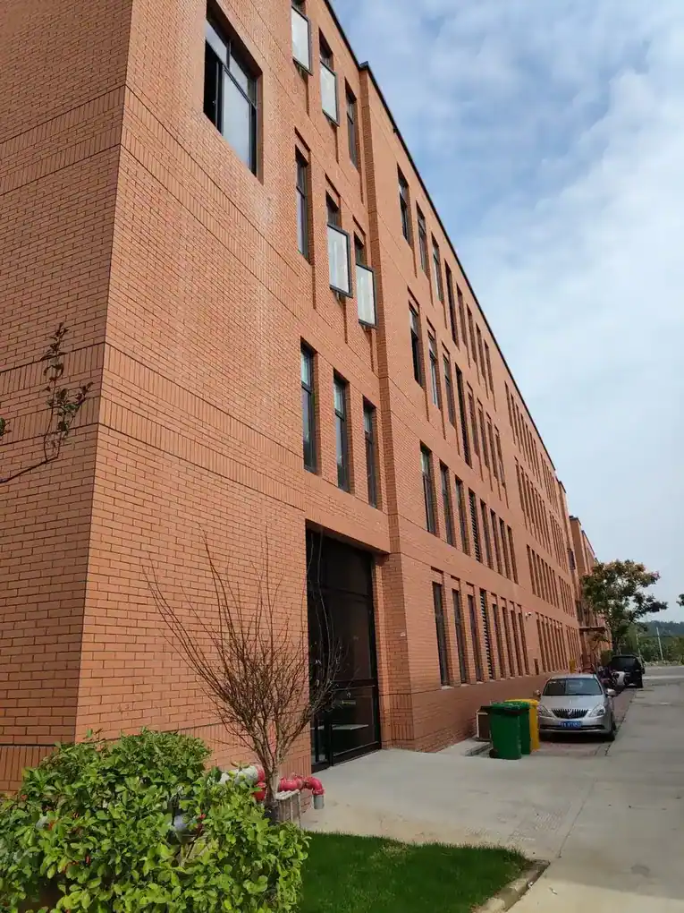 Exterior view of a multi-story red brick industrial building along a paved pathway.