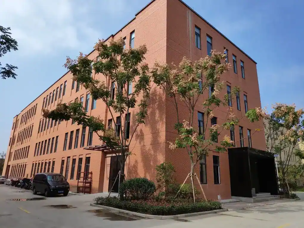 Exterior view of a multi-story industrial facility building with an orange brick facade and landscaping