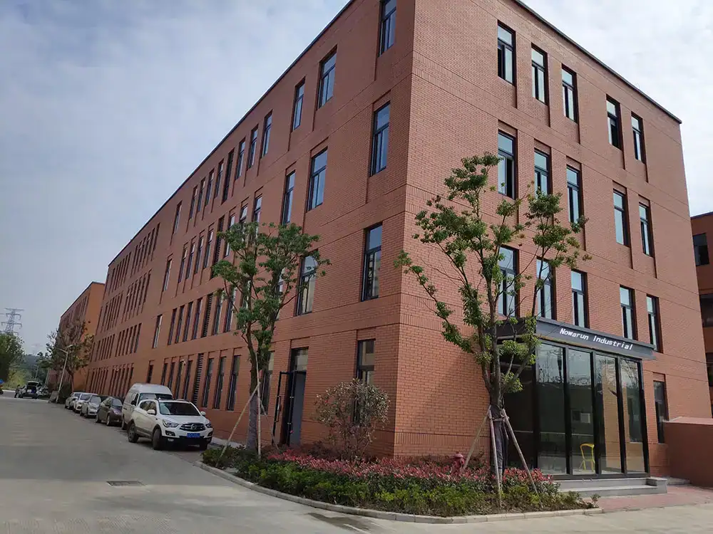 Exterior view of a multi-story red brick industrial building with parked cars along the road