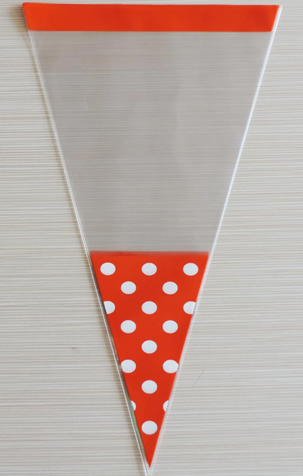 Clear triangular plastic bag with red top and red white polka-dot tip on light background