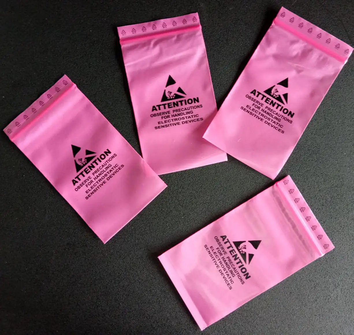 Four pink anti-static ESD bags with handling warning on dark surface