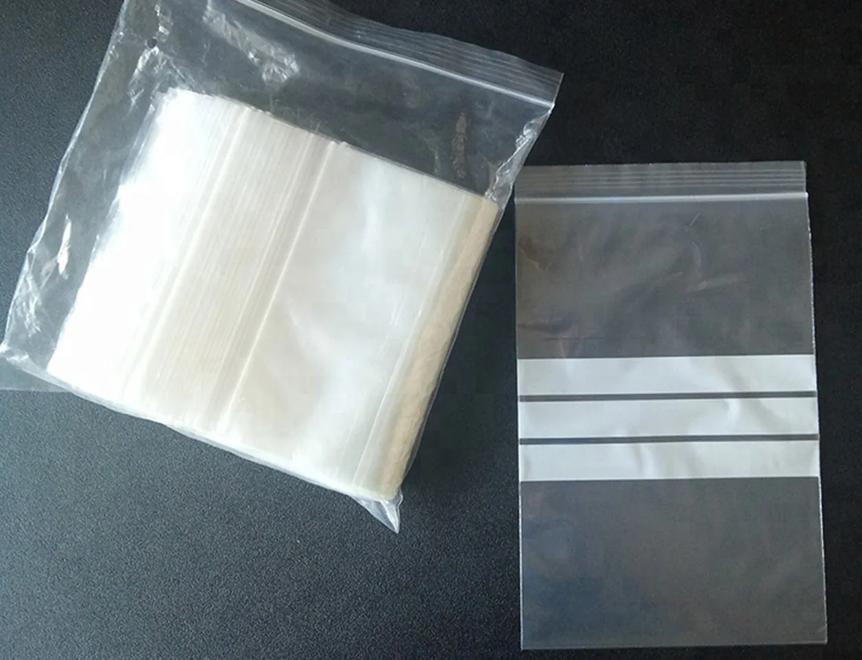 Stack of clear resealable zip bags and one single bag on black surface