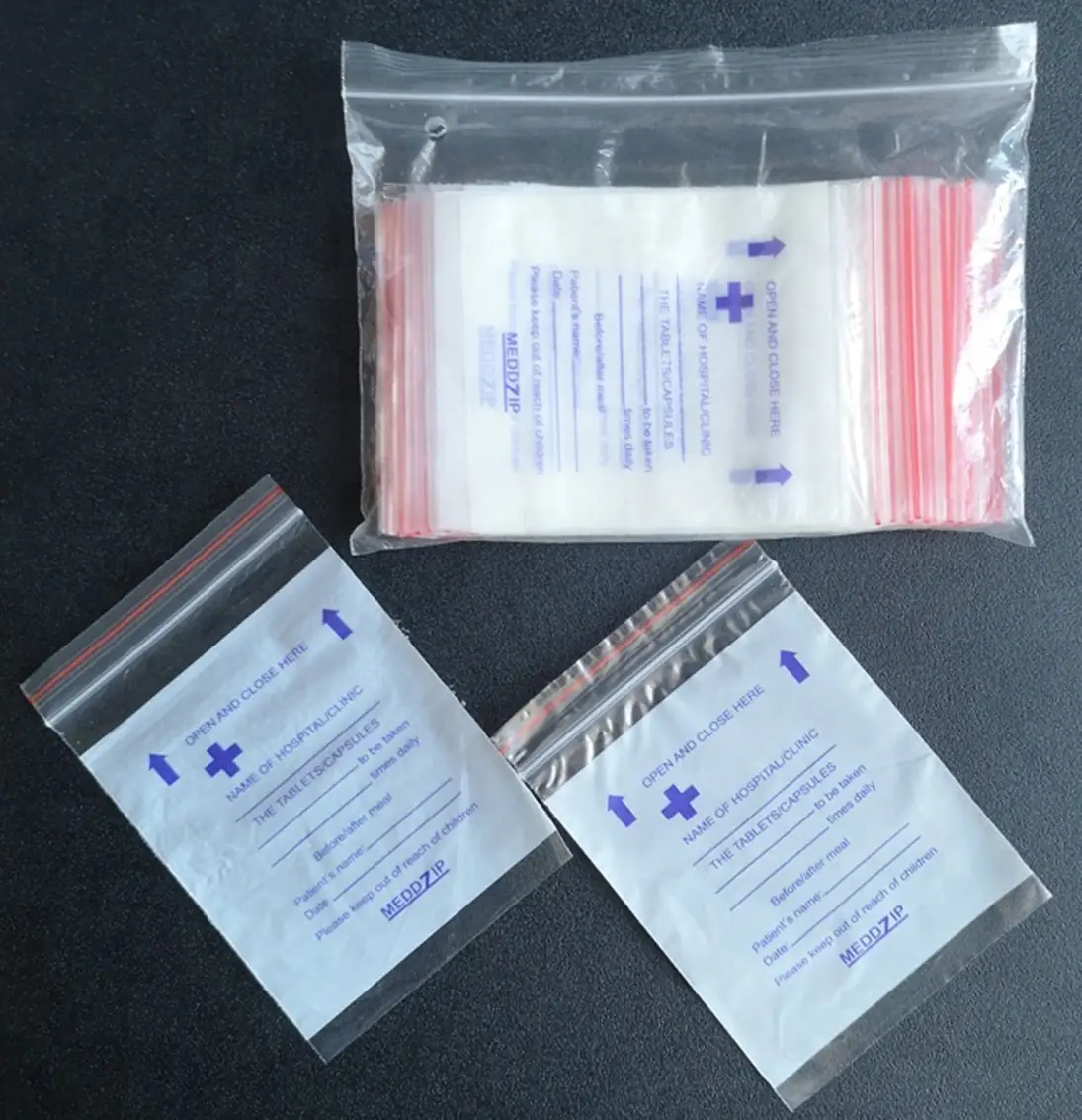 Clear resealable pill bags with blue printing, one pack and two loose bags on dark surface