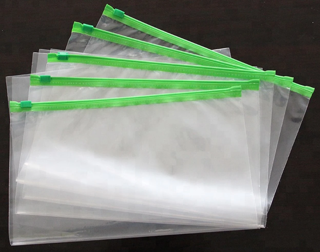 Five transparent resealable plastic bags with green zippers on dark background
