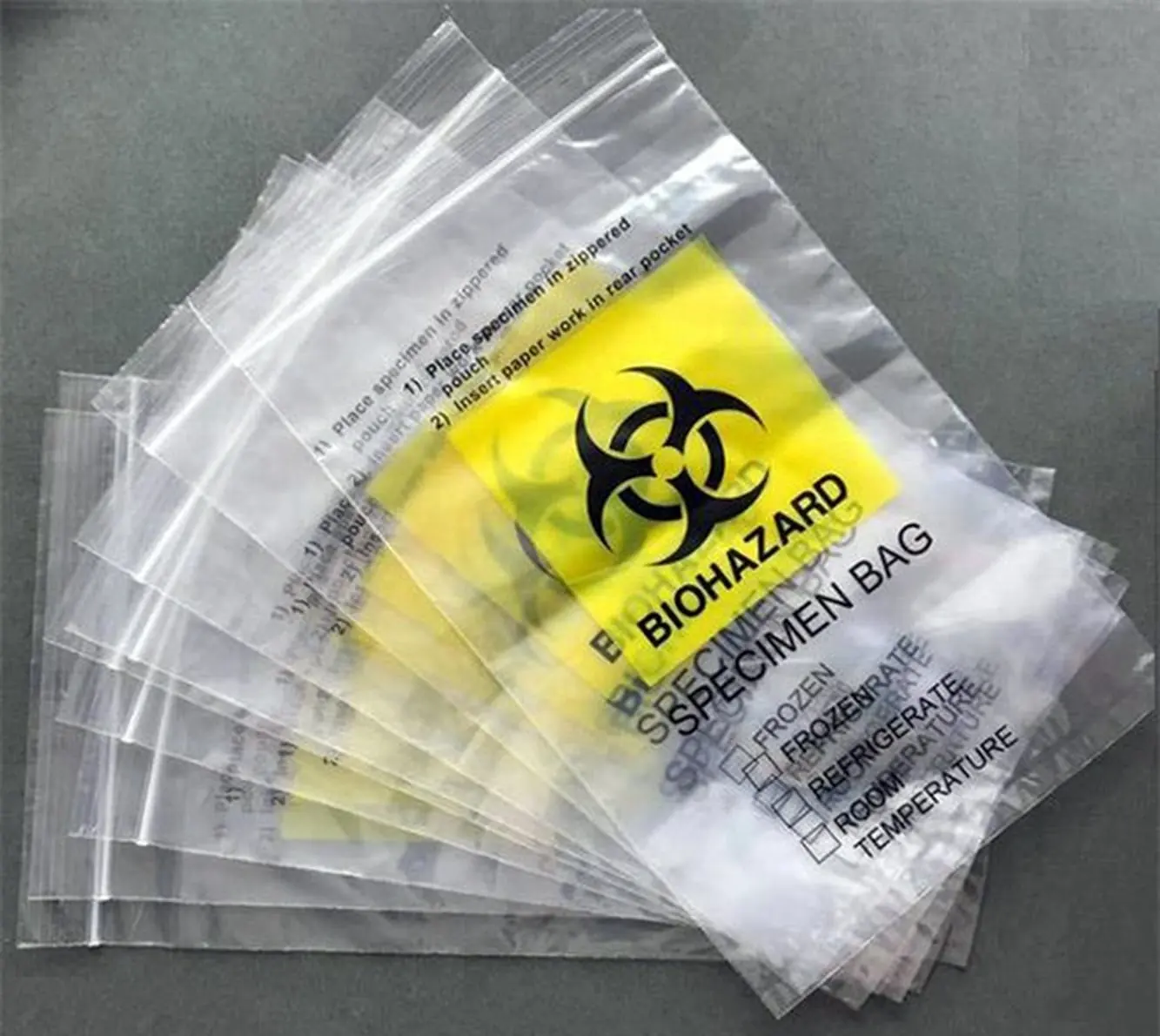Stack of clear plastic biohazard specimen bags with yellow labels on gray surface