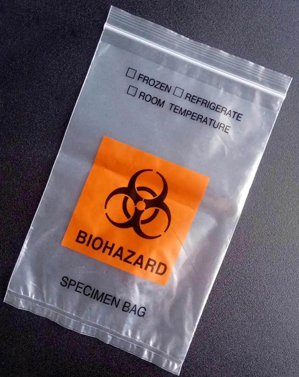 Clear plastic biohazard specimen bag with orange warning label on dark surface