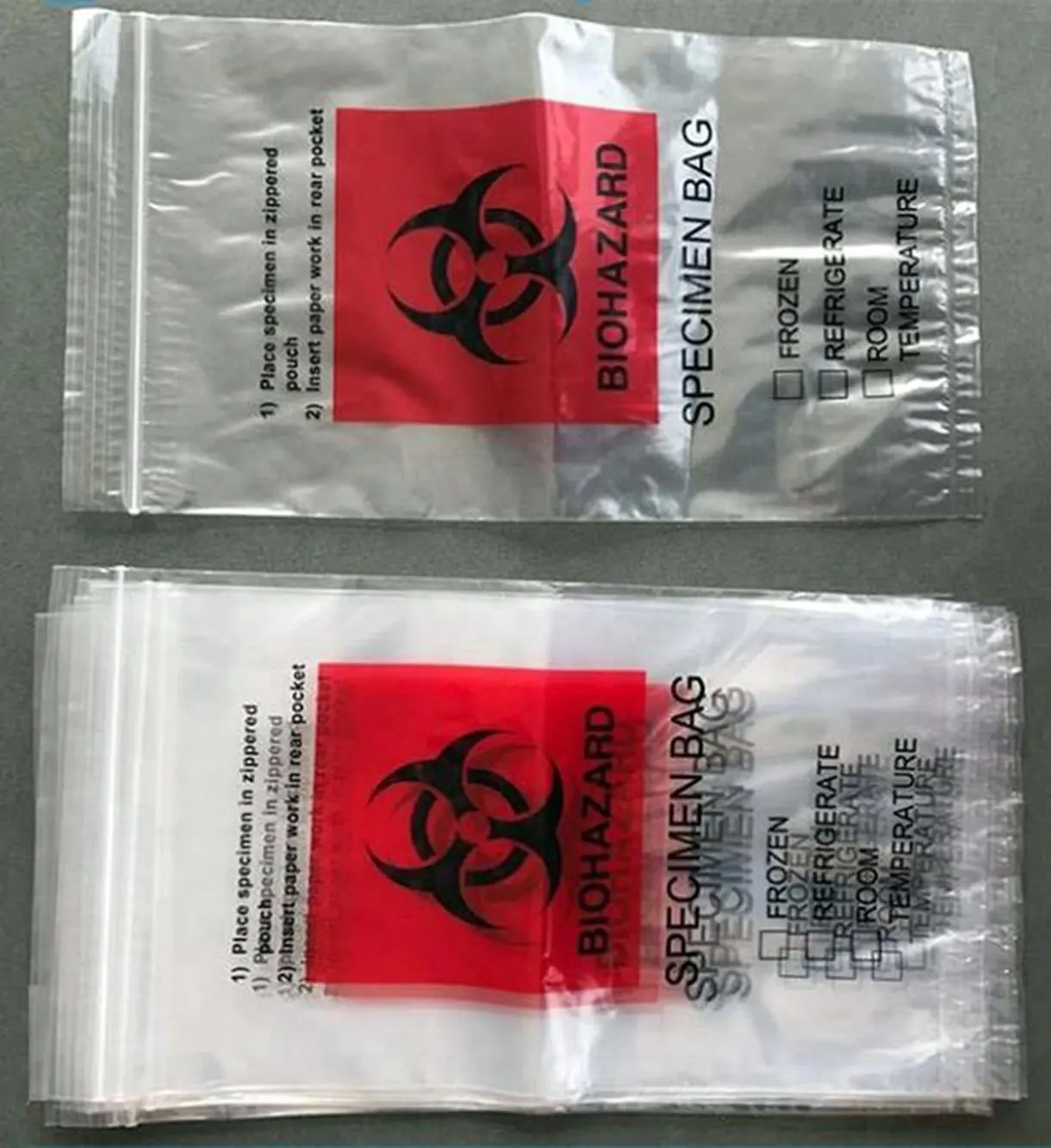 Two clear plastic biohazard specimen bags with red warning labels on gray surface